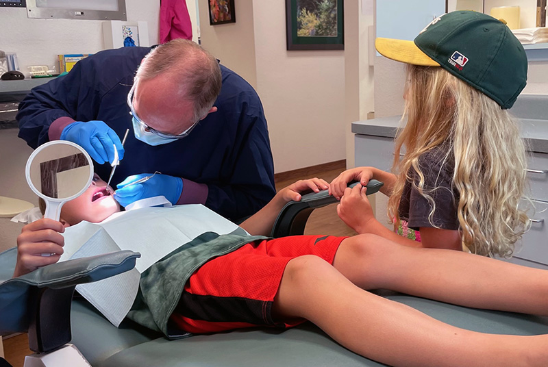 Boy at dental visit with Dr. Heyn with sister standing next to the chair watching.